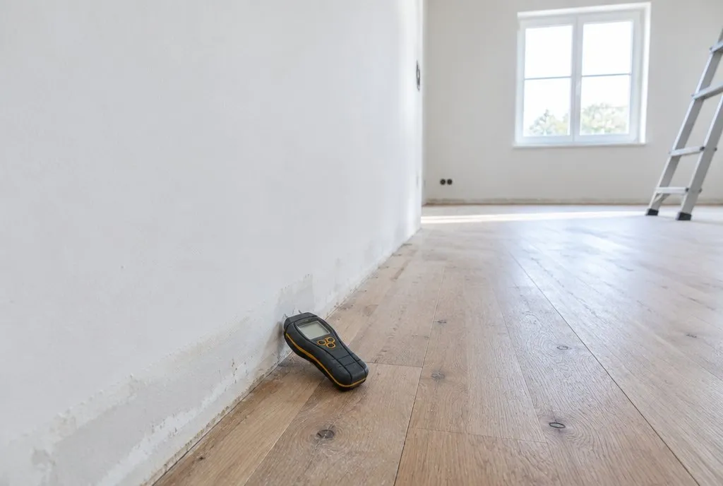 Fugtmåler på gulvet ved en hvid væg i et tomt rum under renovering